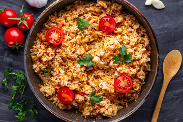 Homemade delicious pilaf with chicken, fresh parsley and ripe vegetables in a pan for lunch on a dark background. Top view