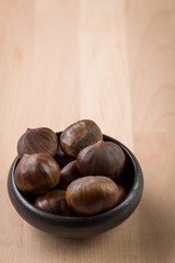 Maronen Esskastanien in schwarzer Schale auf Holz Hintergrund 