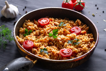 Homemade delicious pilaf with chicken, fresh parsley and ripe vegetables in a pan for lunch on a dark background