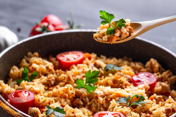 Full pan of homemade delicious pilaf with chicken, fresh parsley and ripe vegetables close up