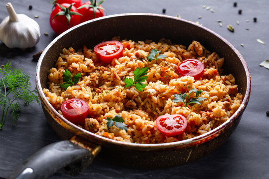 Homemade delicious pilaf with chicken, fresh parsley and ripe vegetables in a pan for lunch on a dark background
