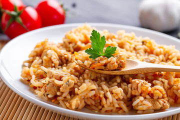 Plate of homemade delicious pilaf with chicken, fresh parsley and ripe vegetables for lunch