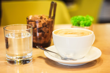 A cup of cappuccino with brown sugar and a glass of water