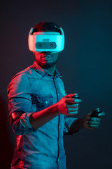 Unrecognizable young African man playing video game wearing virtual reality device against red and blue dual color light on dark background. Gaming equipment for gamers concept.