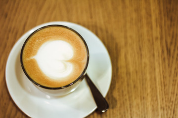 Close up of hot coffee on wooden table at cafe & restaurant, White plate with cup of latte with heart shape latte art. Top view of coffee on cafe background use for food and drink concept. Flat lay