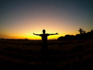 Fototapeta na wymiar Silhouette Asian young man open arm is standing on grass city country home of field with sunset light and beautiful sky twilight sky and cloud. Success, happytime.