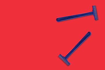 Pair of male disposable plastic razors blue color with two sharp blades on red table in bathroom with copy space for your text. Top view. Hygiene concept