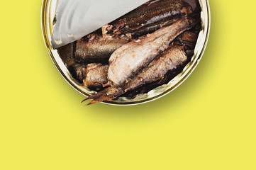 One opened metal can with preserved fish in oil on yellow table on cuisine. Copy space for your...