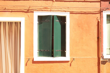 Fototapeta na wymiar Colorful green window with shutters in Mediterranean style on orange wall. Colorful houses in Burano island near Venice, Italy
