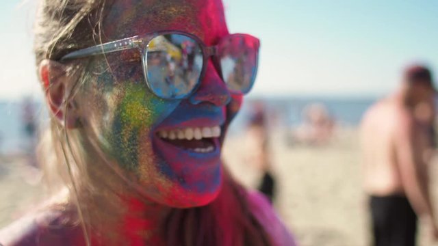 The vacation leisure on the beachline. Female 20s person smile and laugh after the traditional festival holi become from India slow motion. Trendy girl face in mixed colors close up. Happiness and art