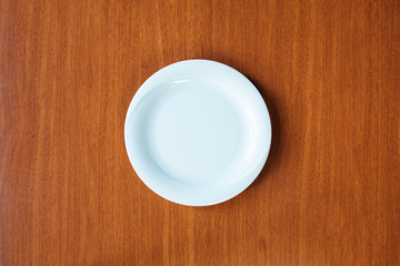 Empty white plate on wooden table from top view