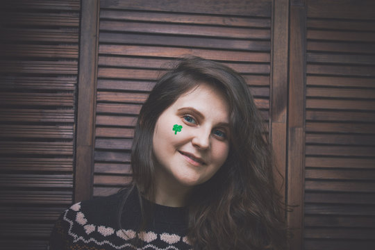 young beautiful woman with painted green clover on her cheek at the bar in front of a wooden wall