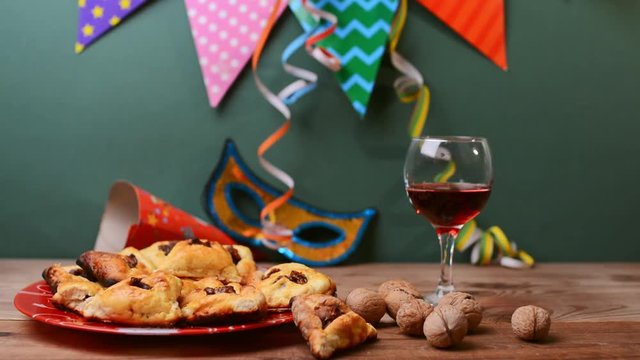 Carnival mask made of gold glitter, Multicolored festive triangular flags and Hamantaschen cookies on table.