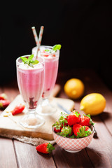 Refreshing milkshakes and bowl with fresh strawberry on wooden table