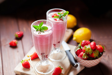 Refreshing milkshakes and bowl with fresh strawberry on wooden table