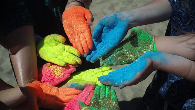 The festival of colors Holi. Hands painted in mixed colors close up. Male and female persons sitting on beachline and doing hindian ritual. Scereny colorful picture of peace and art, summer enjoyment