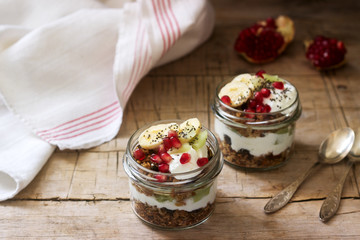Granola with yogurt and fruit in glass jars on a wooden table. Rustic style.