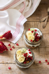 Granola with yogurt and fruit in glass jars on a wooden table. Rustic style.