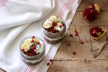 Granola with yogurt and fruit in glass jars on a wooden table. Rustic style.