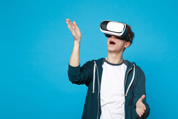 Amazed young man in headset touch something like push click on button, pointing at floating virtual screen isolated on blue background. People sincere emotions, lifestyle concept. Mock up copy space.
