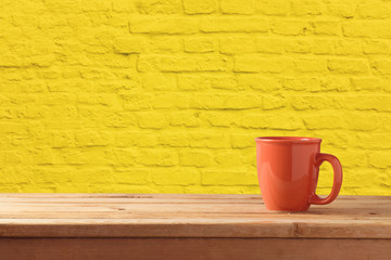 Red coffee or tea cup on wooden table over yellow brick stone wall background.