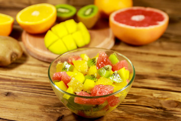 Tasty fruit salad in glass bowl and fresh fruits on the wooden table