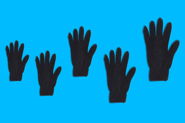 Horizontal row of black warm woolen gloves from small to large on blue background. Top view