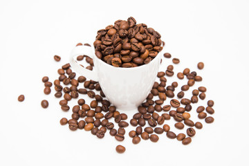 White cup filled with coffee beans with scattered coffee beans on a white background