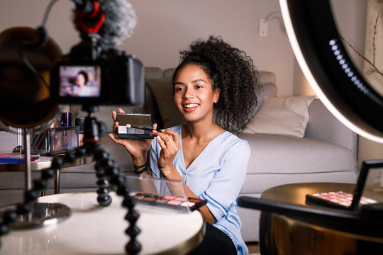 Smiling woman holding a makeup palette while recording her video for blog