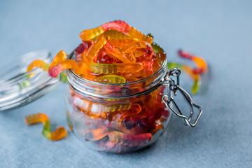 Chewing marmalade in the form of worms in a glass jar. Gummies.