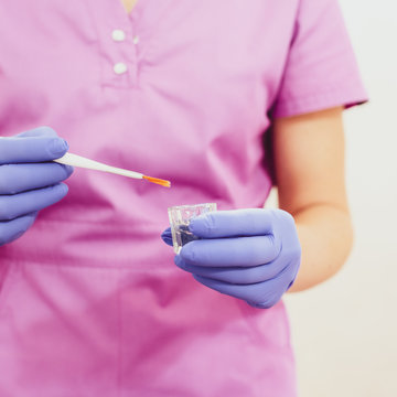Female hands of a beautician with small glass cup and aplicator