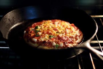 Freshly baked homemade pizza with pepperoni and chopped bell peppers in cast iron pan from the oven.