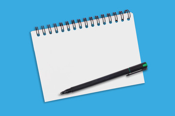 One paper notepad with spiral binder and blank sheets near black plastic pen lies of blue office table. Top view. Copy space for your text. Concept of business or education
