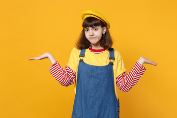Displeased girl teenager in french beret, denim sundress spreading, pointing hands aside isolated...