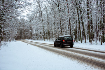 Black car driving through the woods on an asphalt road covered with snow