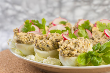 Boiled eggs stuffed with champignon mushrooms and sliced radish, parsley, salad on white plate.