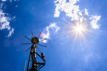 Sun star on a blue sky with some clouds and a weather station in the foreground