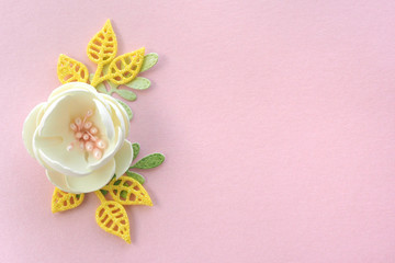 Handmade ivory artificial flower and leaves of yellow and green color on a pink paper background....