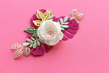 white handmade flower and paper leaves on a pink paper textural background. copy space...