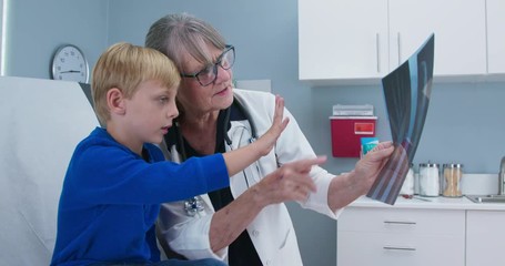 Female senior pediatrician showing x-ray of hand to child patient. Little boy at doctors office. Slow motion 4k - Powered by Adobe