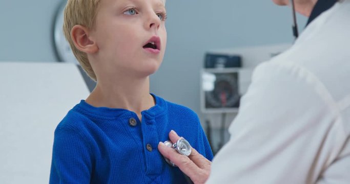 Female pediatrician listening heart of sick little boy using stethoscope. Woman doctor checking heartbeat or breathing of child patient on exam table. Slow motion 4k