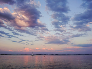 Naklejka na ściany i meble Picturesque river landscape. Sunny sunset. Pink clouds on the blue sky. Sailboat on the horizon.