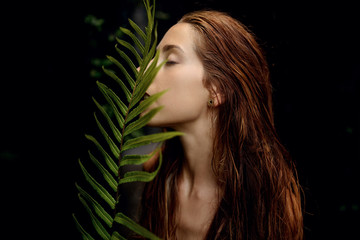 beautiful woman with red hair posing with a fern leaf on dark background