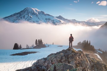 Man on the mountain peak looking on mountain valley with low clouds at colorful sunrise in autumn...