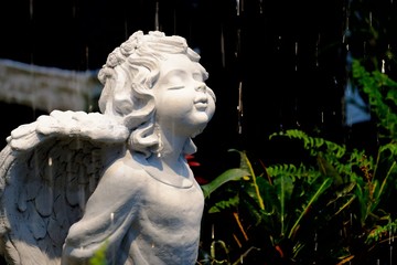 A cute cupid angel statue standing in the garden with rain drops and dark background 