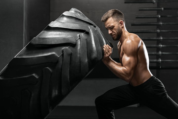 Fototapeta na wymiar Muscular man working out in gym flipping tire, strong male naked torso