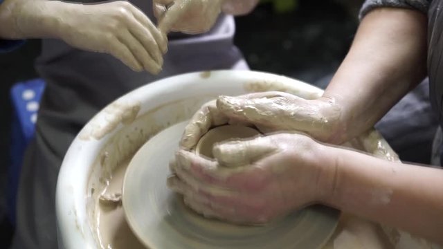 Caring grandma is showing young grandson how to work with clay on throwing-wheel.