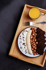 Healthy breakfast bowl and a glass of freshly squeezed orange juice on a wooden tray on a black background.