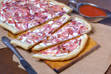 Alsatian tart flambé or Flammkuchen with bacon and onions on a dark table.