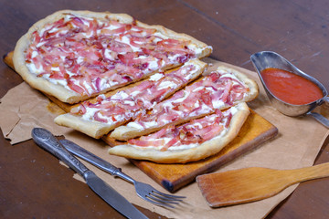 Alsatian tart flambé or Flammkuchen with bacon and onions on a dark table.